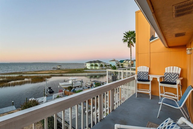 balcony at dusk featuring a water view