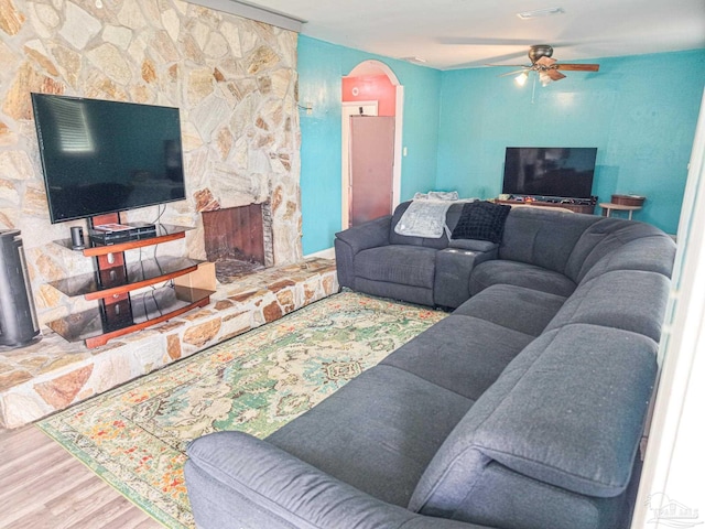 living area with wood finished floors, visible vents, arched walkways, ceiling fan, and a stone fireplace