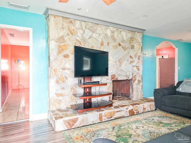 living area featuring arched walkways, visible vents, a stone fireplace, and wood finished floors