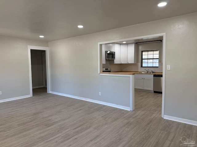 kitchen featuring light countertops, backsplash, appliances with stainless steel finishes, white cabinets, and light wood-type flooring