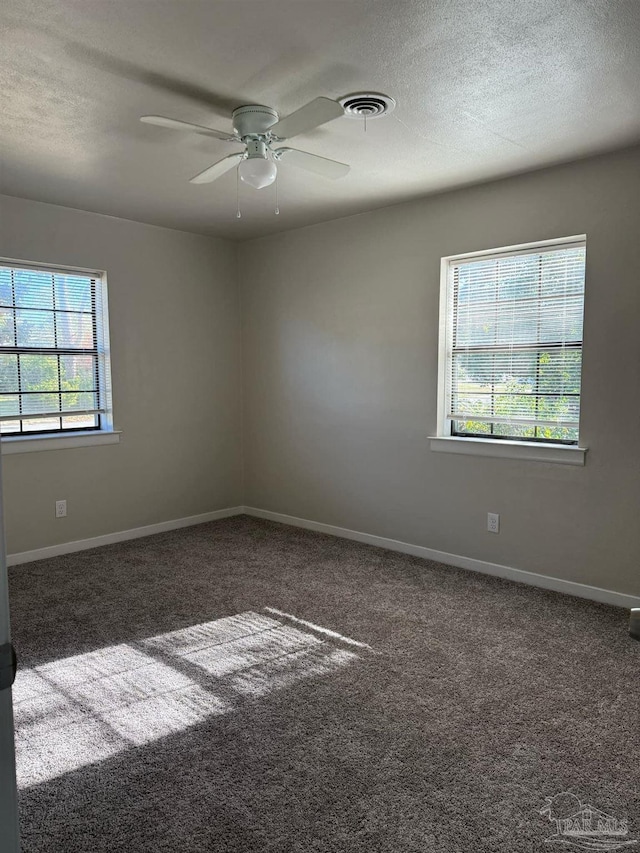spare room with dark colored carpet, visible vents, ceiling fan, a textured ceiling, and baseboards