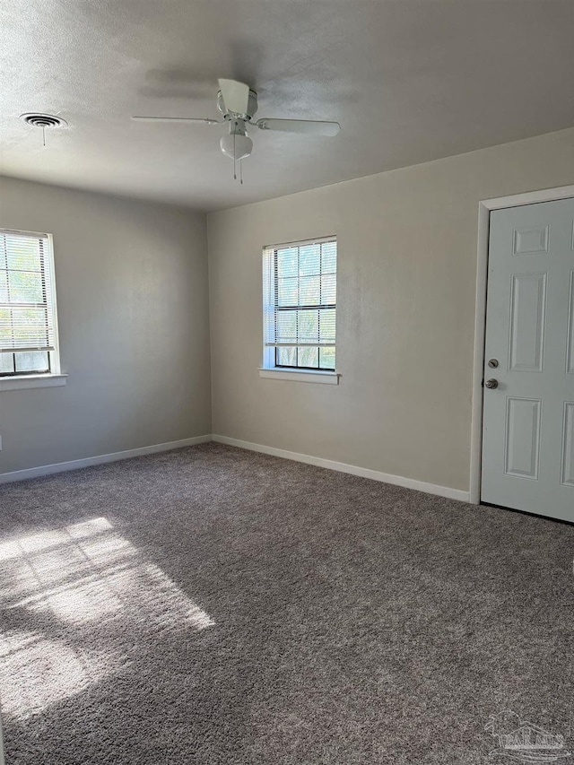 carpeted spare room with a healthy amount of sunlight, a ceiling fan, baseboards, and a textured ceiling