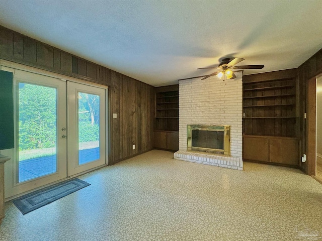 unfurnished living room featuring a textured ceiling, wooden walls, a fireplace, built in features, and french doors