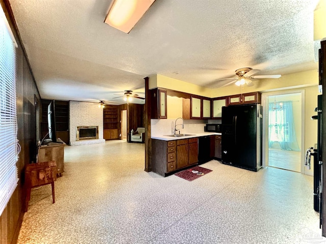 kitchen featuring light countertops, a brick fireplace, open floor plan, a sink, and black appliances