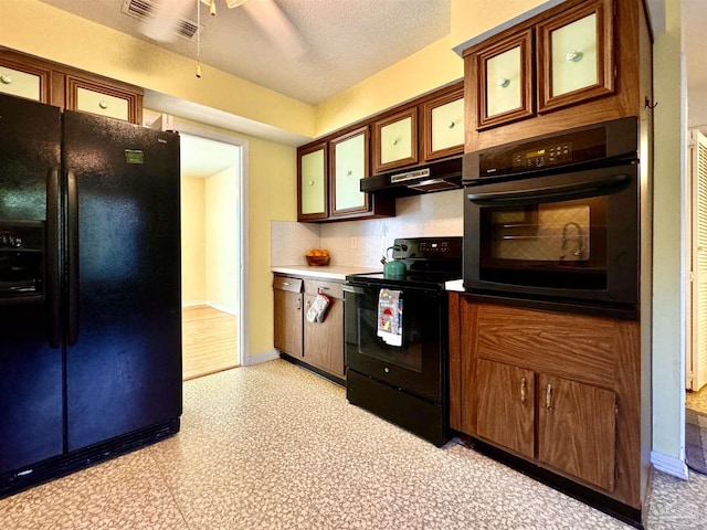 kitchen featuring glass insert cabinets, light floors, under cabinet range hood, a textured ceiling, and black appliances