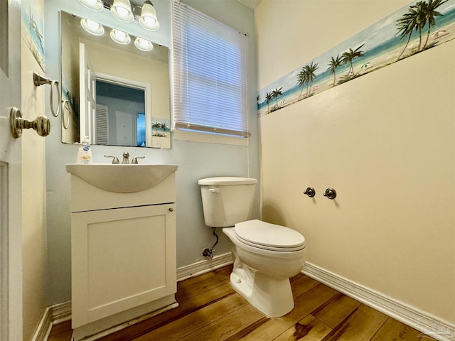 half bath with baseboards, vanity, toilet, and wood finished floors