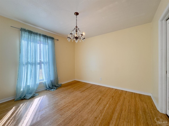 spare room with a notable chandelier, baseboards, and light wood-style floors