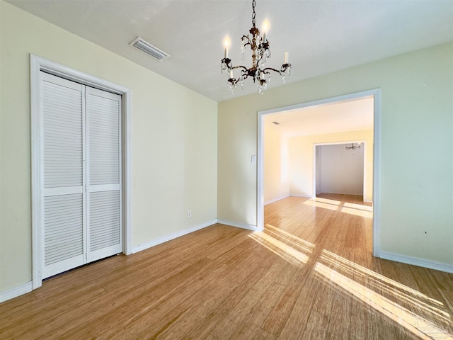 empty room featuring baseboards, an inviting chandelier, visible vents, and light wood-style floors