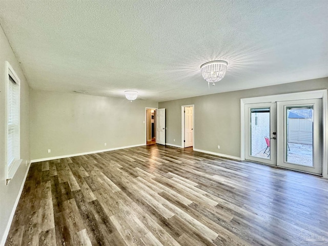 empty room featuring a textured ceiling, a notable chandelier, wood finished floors, baseboards, and french doors