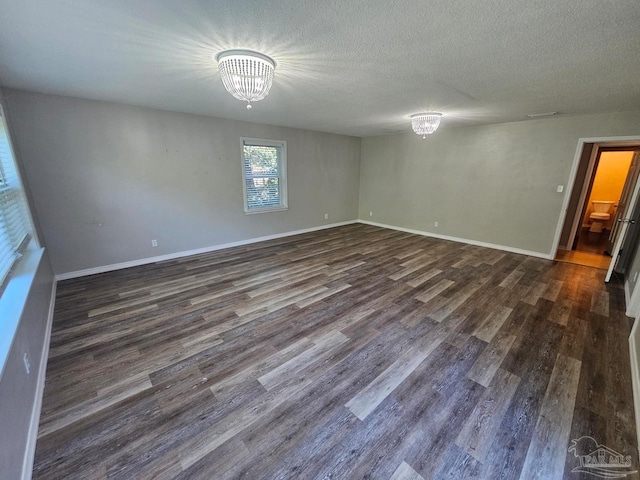 spare room featuring baseboards, dark wood-style flooring, and an inviting chandelier