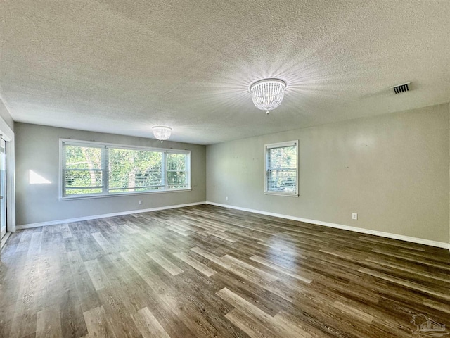 spare room with a notable chandelier, visible vents, a textured ceiling, wood finished floors, and baseboards