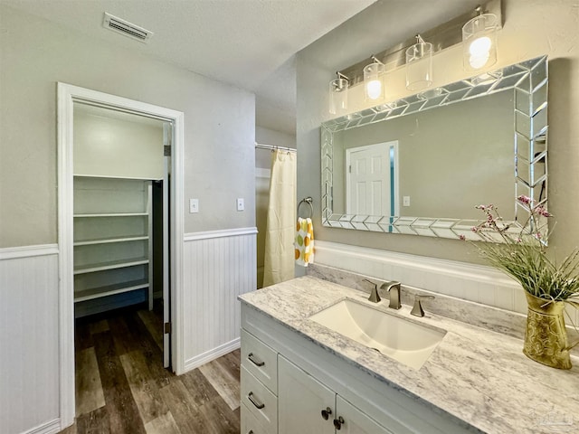 bathroom featuring a textured ceiling, a wainscoted wall, wood finished floors, vanity, and visible vents