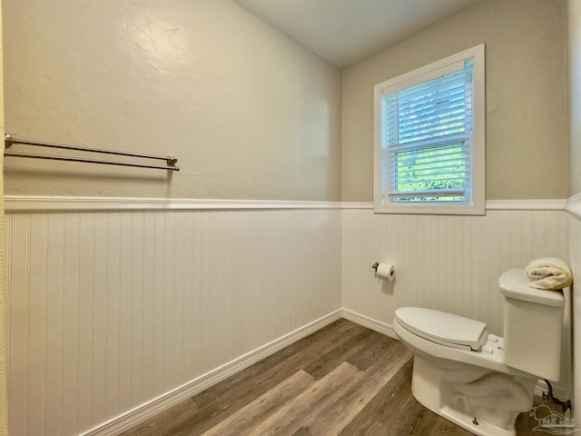 half bath with toilet, wood finished floors, and wainscoting