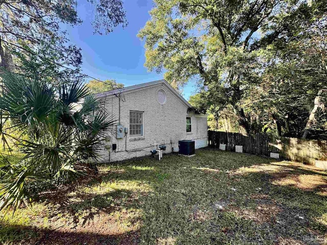 view of side of property with central AC, fence, brick siding, and a lawn