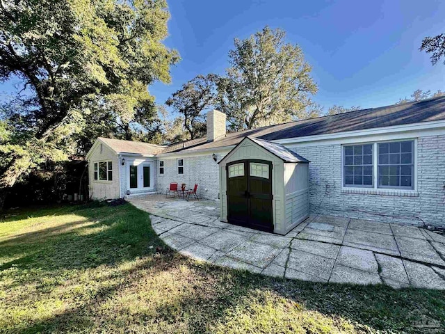 rear view of house with an outdoor structure, french doors, a lawn, a chimney, and a patio area