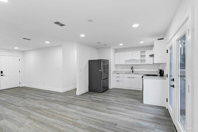 kitchen with stainless steel refrigerator, sink, stove, white cabinets, and light wood-type flooring