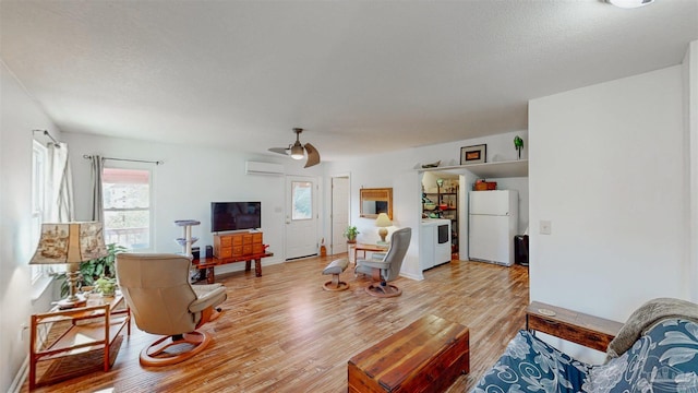 living area featuring a textured ceiling, a ceiling fan, an AC wall unit, light wood finished floors, and washer / dryer