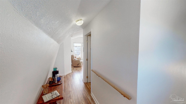 hallway featuring light wood-style flooring, baseboards, vaulted ceiling, and a textured ceiling