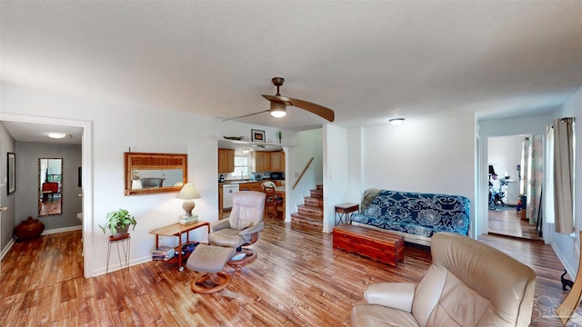 living area with light wood-style flooring, stairway, ceiling fan, and baseboards