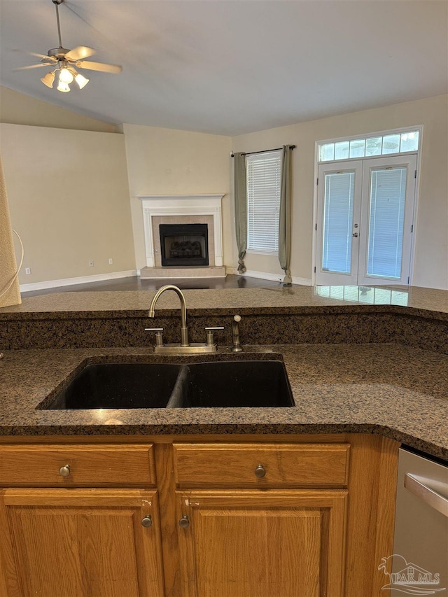 kitchen featuring brown cabinets, a sink, dark stone countertops, a fireplace, and dishwasher