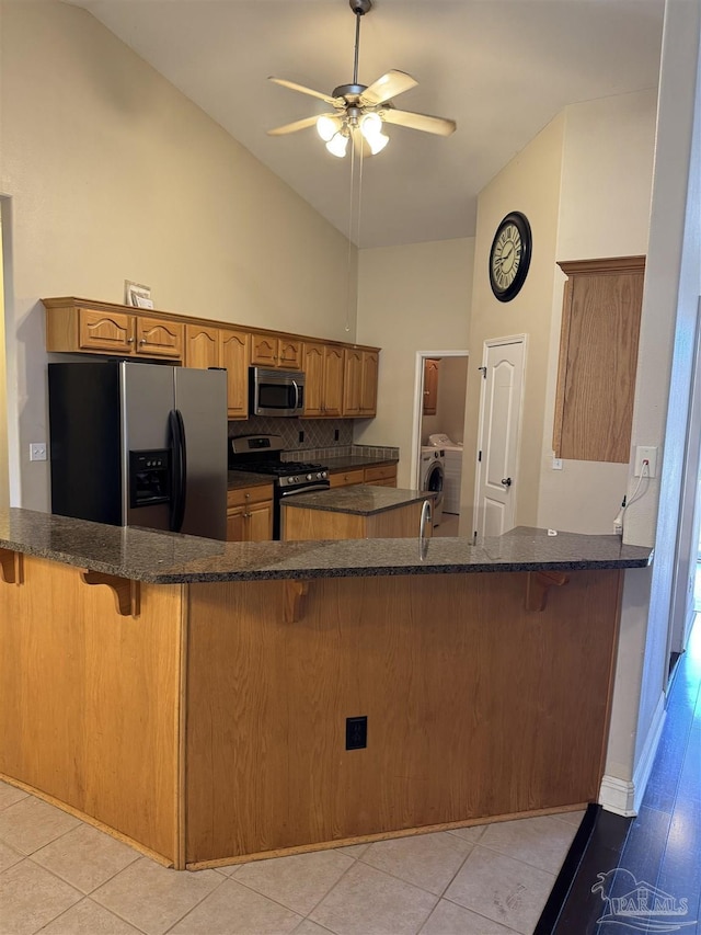 kitchen with dark stone counters, brown cabinets, a kitchen breakfast bar, appliances with stainless steel finishes, and washer / clothes dryer