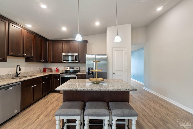 kitchen with a sink, a breakfast bar area, dark brown cabinetry, baseboards, and appliances with stainless steel finishes