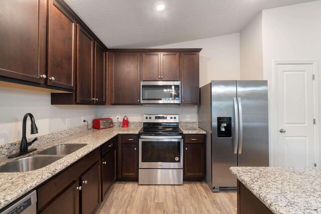 kitchen featuring stainless steel appliances, light wood-style flooring, a sink, dark brown cabinetry, and lofted ceiling