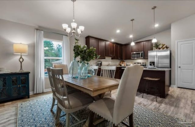 dining space featuring light wood-style floors, vaulted ceiling, baseboards, and a notable chandelier