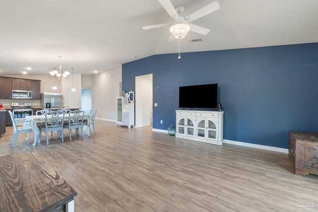 living area featuring vaulted ceiling, ceiling fan with notable chandelier, light wood finished floors, baseboards, and visible vents