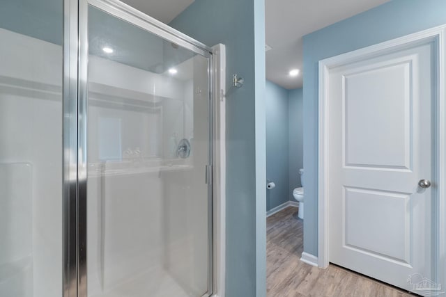 bathroom with toilet, baseboards, wood finished floors, and a stall shower