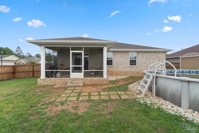 rear view of house with a fenced in pool, a fenced backyard, brick siding, a lawn, and a sunroom