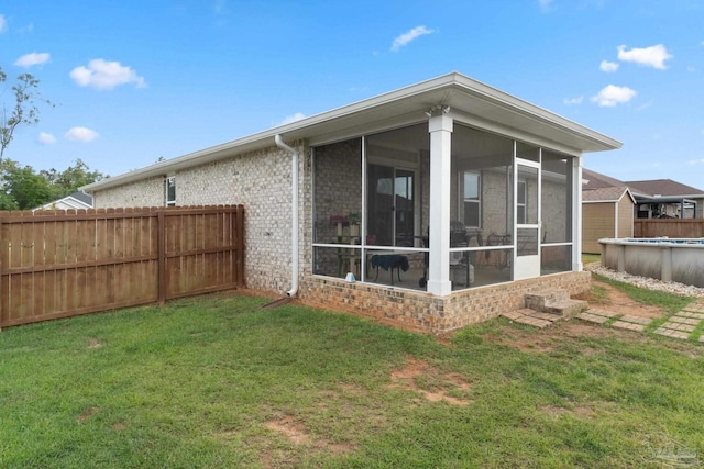 rear view of house with brick siding, a lawn, fence, a fenced in pool, and a sunroom