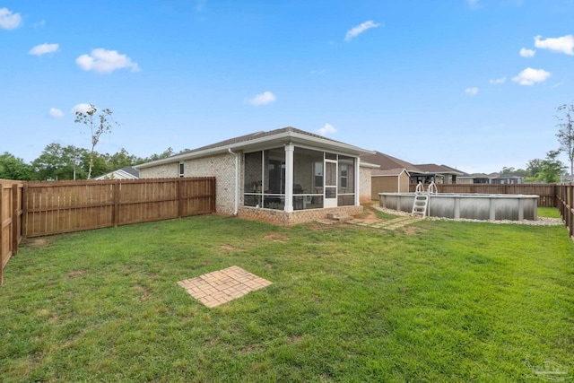rear view of house featuring a lawn, a fenced backyard, a fenced in pool, brick siding, and a sunroom