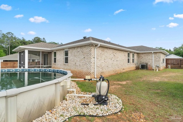 rear view of property with central AC unit, a lawn, fence, brick siding, and a sunroom