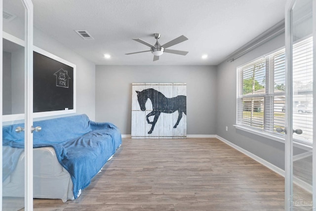 living area with baseboards, wood finished floors, visible vents, and ceiling fan