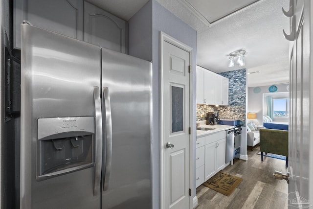 kitchen with white cabinetry, wood-type flooring, backsplash, stainless steel appliances, and a textured ceiling