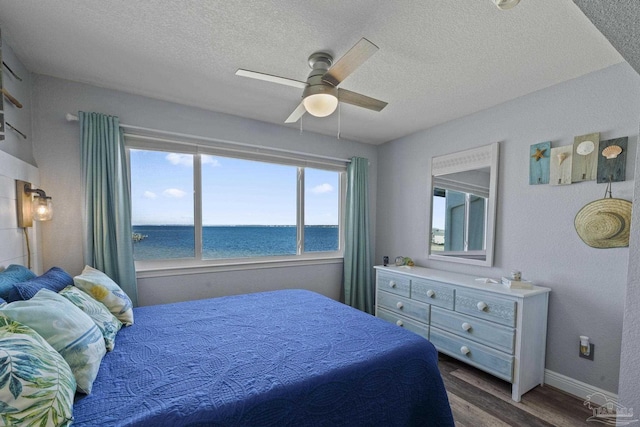 bedroom featuring ceiling fan, dark hardwood / wood-style floors, a textured ceiling, and a water view