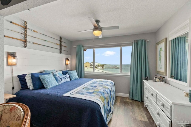 bedroom with hardwood / wood-style flooring, ceiling fan, a water view, and a textured ceiling