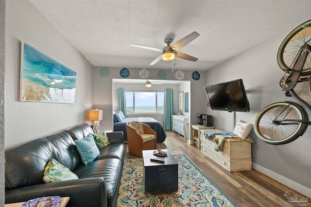 living room featuring ceiling fan, wood-type flooring, and a textured ceiling