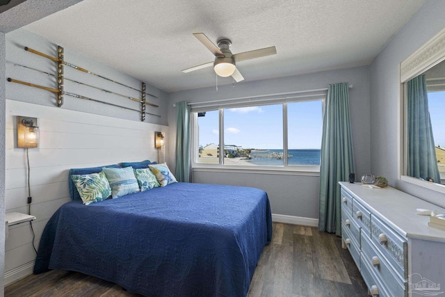 bedroom featuring ceiling fan, a water view, dark wood-type flooring, and a textured ceiling