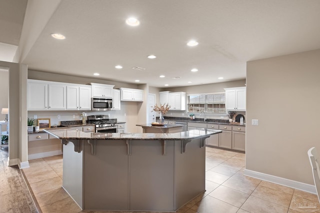 kitchen featuring a breakfast bar, stainless steel appliances, a spacious island, white cabinets, and dark stone counters