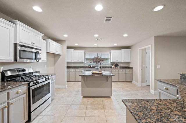 kitchen featuring white cabinetry, appliances with stainless steel finishes, dark stone countertops, and light tile patterned floors