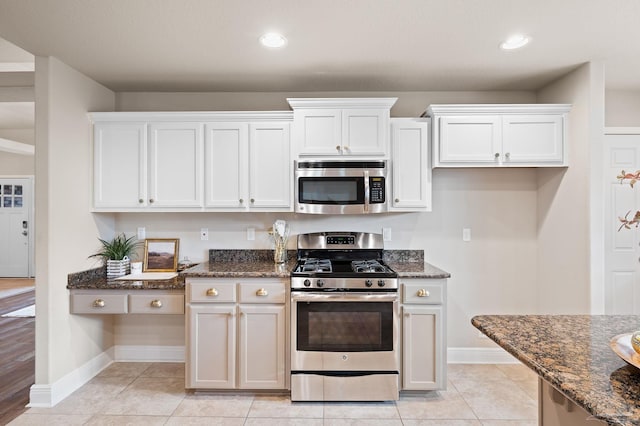 kitchen with dark stone countertops, appliances with stainless steel finishes, light tile patterned floors, and white cabinets