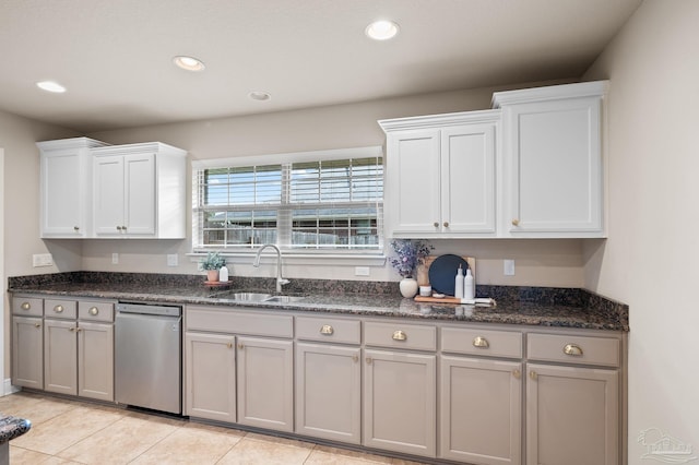 kitchen featuring sink, light tile patterned floors, white cabinetry, stainless steel dishwasher, and dark stone counters