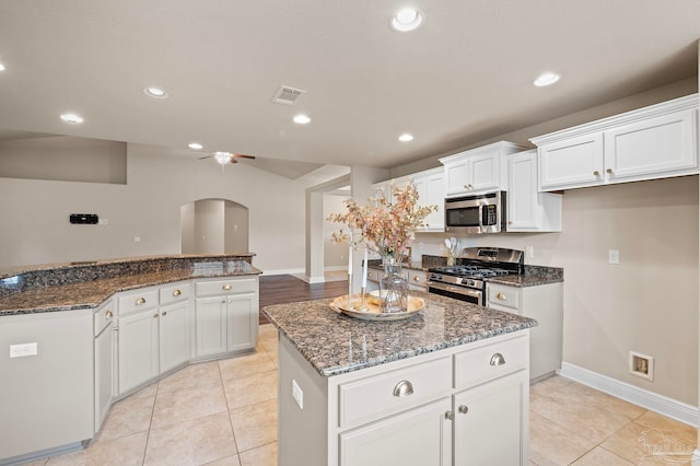 kitchen featuring white cabinetry, a center island, appliances with stainless steel finishes, ceiling fan, and dark stone counters