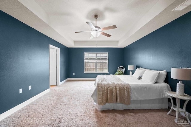 carpeted bedroom featuring ceiling fan and a tray ceiling