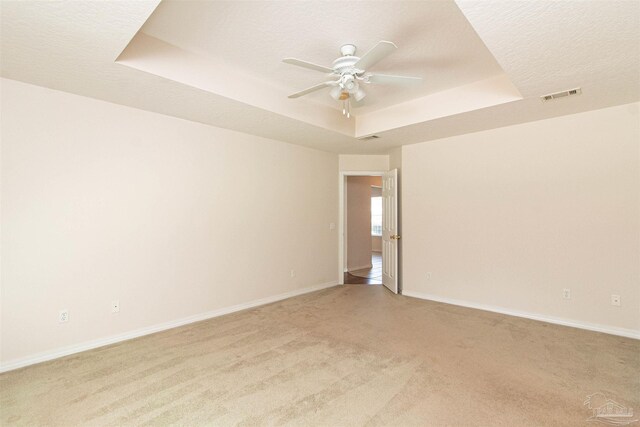 unfurnished room featuring ceiling fan, light colored carpet, a textured ceiling, and a raised ceiling