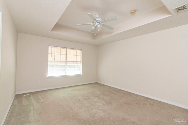 spare room with light carpet, a tray ceiling, and ceiling fan