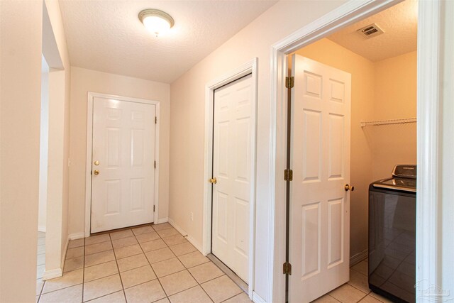 corridor with a textured ceiling, light tile patterned floors, and washer / dryer