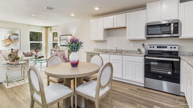 kitchen with appliances with stainless steel finishes, light wood-style floors, white cabinets, and a sink